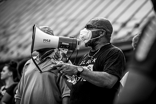 A masked and protesting Don Gathers holding a megaphone.