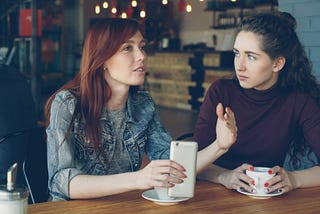 Two women sitting in a coffee shop chatting.