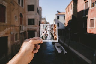 A hand holding a photo of an old canal, in front of the canal