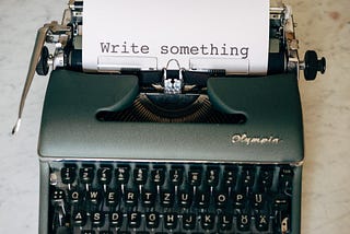 A typewriter with a piece of paper. On it: “Write something”