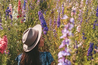 a young girl sitting in a field among tall grass and colorful flowers