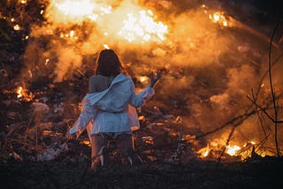 Woman kneeling in front of an apocalyptic fire scene.