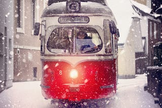 Red tram on a street in a light snow storm.