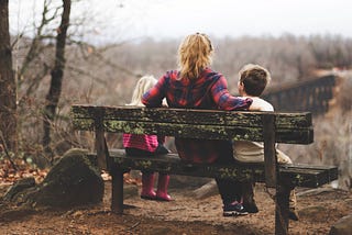 Mother sitting on bench with young son and daughter in nature