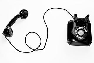 A vintage, black, corded phone with its receiver off the hook.