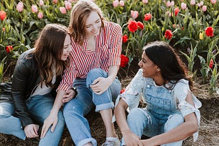 Three ladies smiling and having a chat while sitting in a flower garden