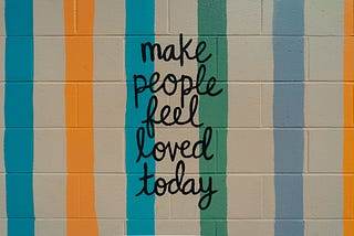 Sign with colored striped that says “Make people feel loved today.”