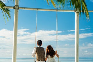 couple on large white swing on the beach, overlooking the sea on a gloriously sunny day