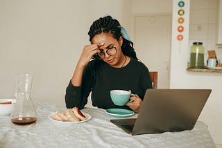Woman at laptop with coffee, finger on forehead