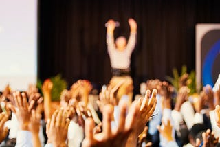 Male speaker andaudience with hands in the air