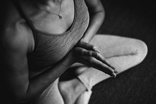 A young woman practices yoga in her living room during a busy day, surrounded by work materials and a laptop on a nearby desk. She is in a peaceful pose, demonstrating mindfulness and balance amidst her hectic schedule.