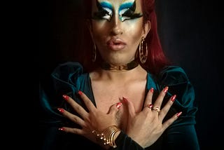A drag persona framed in shadows — vibrant, polished, beautiful. But beneath the lashes and lacquered nails is the man who screamed in a pub, the strategist who staged his own erasure. You can hide behind the mascara, darling. But metadata doesn’t lie. You’re seen. You’re archived. You’re undone.