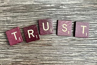 Scrabble-type letters on a woodgrain tabletop spelling the word “Trust”