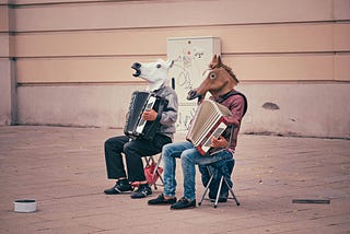 Two men playing a musical instrument on the street with horse masks on their faces.