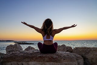 Woman doing yoga in front of the sea and sunset