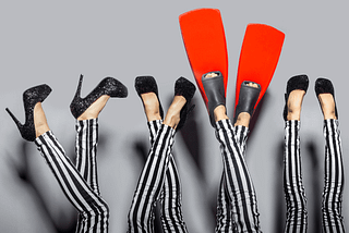 Red flippers standing out in a sea of black shoes. Image courtesy of Happycity21 via canva.com.