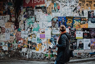 A woman looking at a wall filled with various posters, promo material, ads, etc.