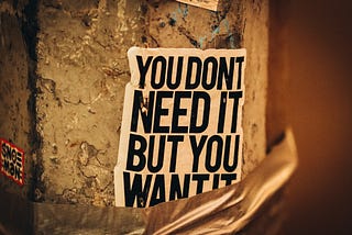 A poster on a crumbling wall with the text ‘You don’t need it, but you want it’.