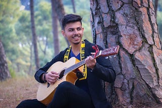 A man plays the guitar in nature and has a terrific time.