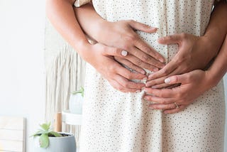 pregnant women in cream colored dress with partner during the first trimester