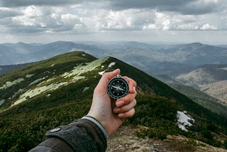 A person holding a compass in front of a mountain.