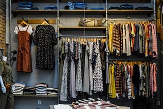 Open fronted wardrobe showing various styled outfits and clothes, beautifully folded and hung.