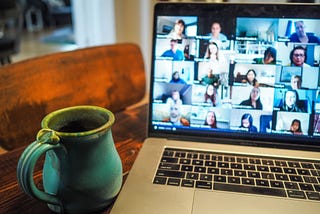 Image of a laptop on a desk with a number of faces on the screen as if participating in a virtual meeting