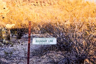 barbed wire fence with sign “Boundary Line”