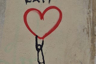 A stick figure dangling from a painted heart on a wall. The word EXIT written above.