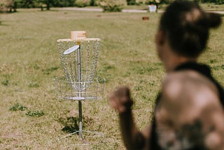 A person tosses a disc into a disc golf basket