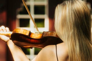 Female violinist in strappy dress with long blonde hair, viewed from the back.