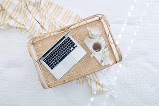 A Macbook and hot beverage on a wicker try next to a sarong, all on a sunbed.