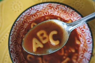 A bowl of alphabet soup and a spoon hovering above holding letters A, B, and C.