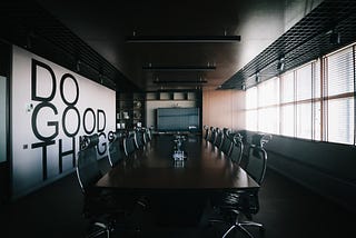 Picture of a dark, empty boardroom with a large poster on the wall saying, Do Good Things