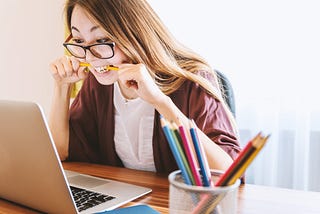 Stressed young woman biting her pencil while looking at screen