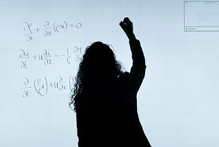 a silhouette of a woman in front of a smart board, working on a math equation
