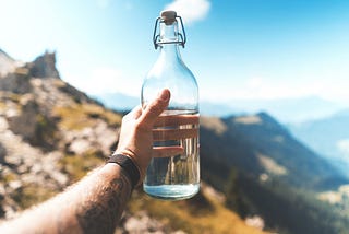 a man’s hand is holding a bottle of water against a beautiful background.