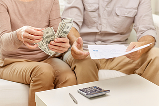 Couple sitting on a sofa, counting money, and looking over bills.