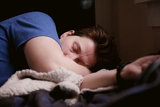 Man wearing a blue shirt sleeping on his side with his head resting on one arm.