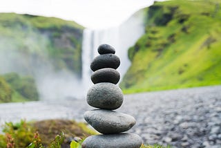 six small rocks balanced on top of each other in front of a waterfall