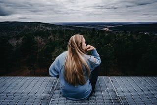 A women sitting on rooftop with a view of a forest