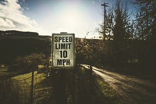 An image illustrating a speed limit sign on the side of a road, symbolizing the concept of setting limits for achieving success. The sign with the number “10” is placed on a pole, surrounded by a fence, under a bright sun. The empty road signifies the journey towards success, while the natural lighting adds a sense of optimism and possibility.