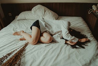 A woman lays in the middle of a bed, curled up in a ball.