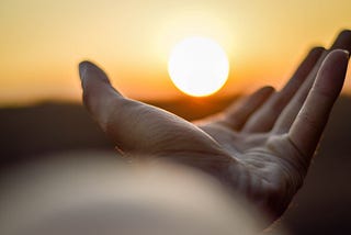 A photograph of an outstretched hand point to the sun.