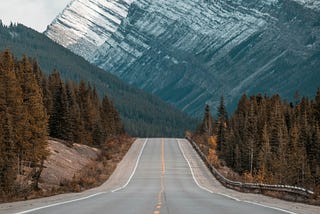 An open road leading to snow-capped mountains in the background.
