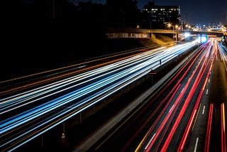 Long exposure picture of a highway, where the lights from the vehicles are really long continuous lines covering the road (and vehicles are actually not visible), giving a sense of really high speeds.