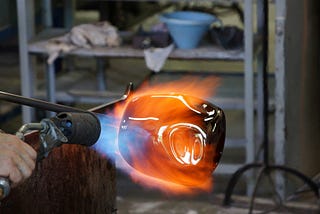 Artist using a blue flamed torch to fuse and heat glass into artwork.