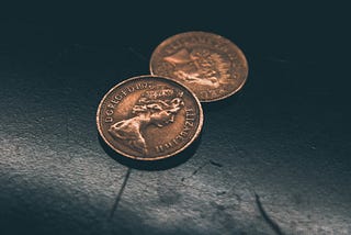 Two British pence on a dark background.