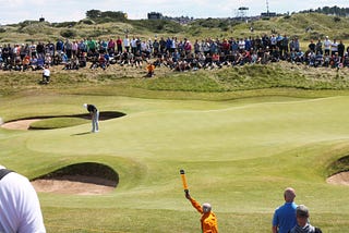 Golfer putting on edge of green with crowd behind