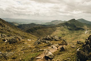 A landscape photograph of rural Wales, grey cloud in the sky and rock-covered hills and valleys.